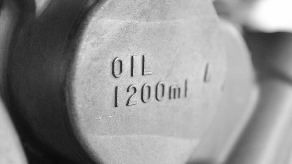 金属パーツに「OIL 1200ml」と刻印された給油口のモノクロ写真。機械の潤滑油漏れを防ぐオイルシールの重要性と、交換時期・選び方を解説する記事のアイキャッチ。