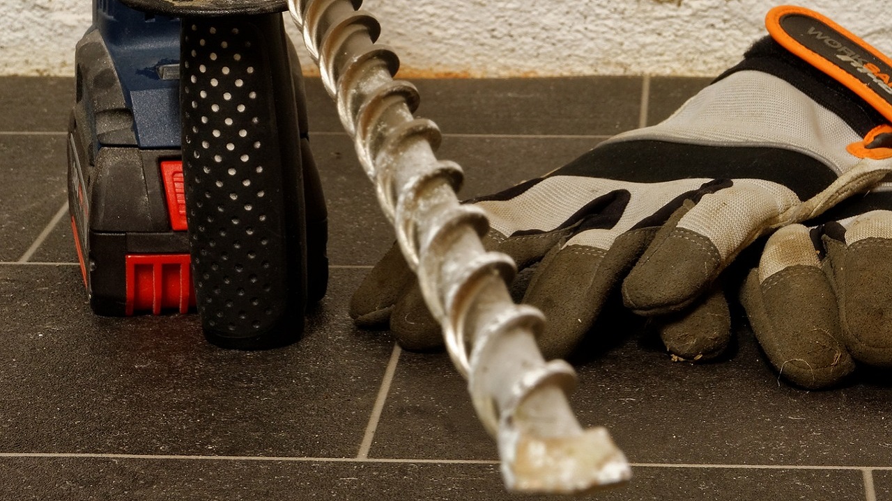 コンクリート穴あけ用のハンマードリルと太いドリルビット、作業用手袋のイメージ写真